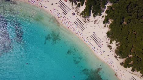 Drone-orbiting-while-slowly-descending-down-the-beachfront-of-Cala-Agulla,-showing-the-crystal-clear-blue-waters-and-sandy-beaches-in-Llevant-Peninsula-in-the-island-of-Mallorca-in-Spain