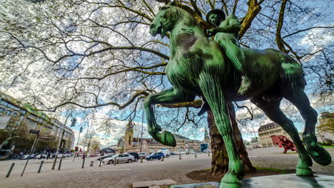 Timelapse-shot-of-a-statue-of-man-riding-a-hose-with-traffic-passing-by-in-Hamburg,-Germany-at-daytime