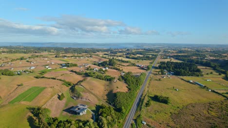 Aerial-ascending-shot-of-a-road-in-middle-of-farmlands-of-sunny-Chiloe,-Chile