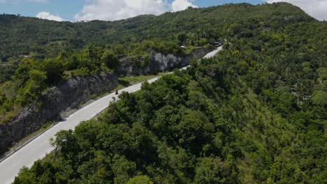 A-winding-road-on-cebu-island-with-lush-greenery-and-moving-scooters,-aerial-view