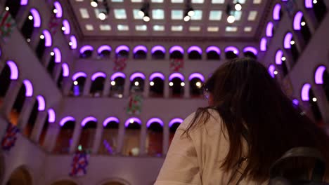 Low-angle-view-woman-observing-illuminated-Fondaco-dei-Tedeschi-arches-in-a-purple-hue