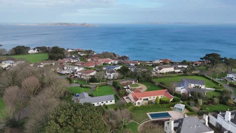 Vuelo-Sobre-Fort-George,-Una-De-Las-Urbanizaciones-Más-Caras-De-Guernsey,-Hacia-El-Mar-Con-Vistas-A-Herm-Sark-Y-Jethou-En-Un-Día-Soleado
