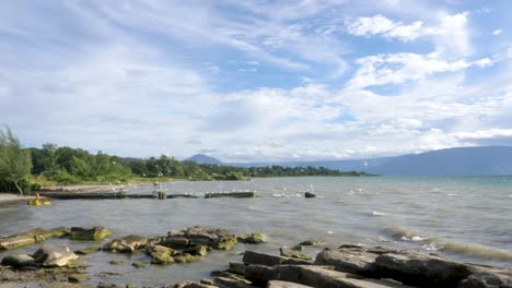 Lake-Toba-shoreline-with-white-storks,-lush-greenery,-and-calm-waters-under-a-partly-cloudy-sky,-daytime