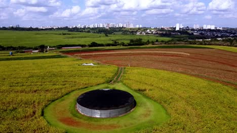 Aerial-view,-water-tank-and-a-cornfield,-with-city-of-Campo-Grande-background