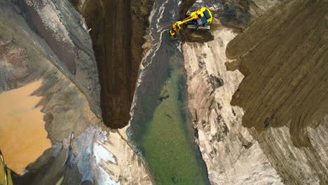 Una-Excavadora-Manejando-Sedimentos-En-Un-Estanque-De-Secado,-Rodeado-De-Altos-Muros-De-Tierra,-Vista-Aérea