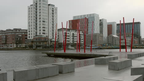 Modern-waterfront-of-Dublin-Docklands-with-red-sculptures,-urban-architecture,-on-overcast-day