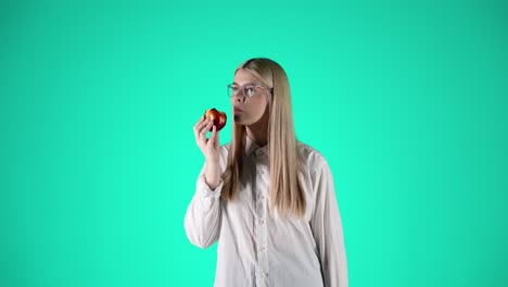 Beautiful-young-woman-enjoys-a-red-juicy-apple,-turquoise-background,-studio