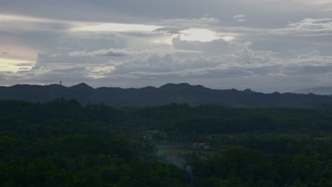 Misty-dawn-over-the-Chocolate-Hills-in-Bohol,-Philippines,-with-soft-sunlight-piercing-clouds