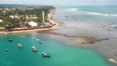 Aerial-view-of-Praia-do-Forte-beach,-the-coral-reef,-boats-parked,-palm-tree-area-on-a-cloudy-day,-Praia-do-Forte,-Bahia,-Brazil