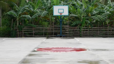 Cancha-De-Baloncesto-Al-Aire-Libre-En-Filipinas-Con-Un-Aro-Azul,-Rodeada-De-Exuberante-Vegetación-Y-Cielo-Nublado