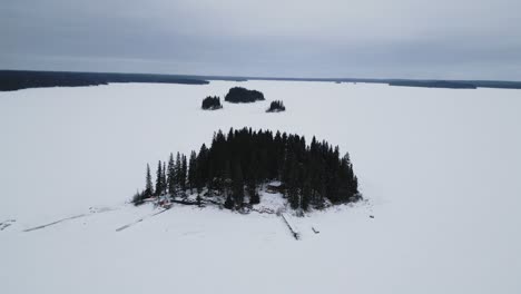 A-Rising-Drone-Shot-of-an-Island-on-Frozen-Canadian-Paint-Lake-with-an-Ice-fishing-hut-and-skioos