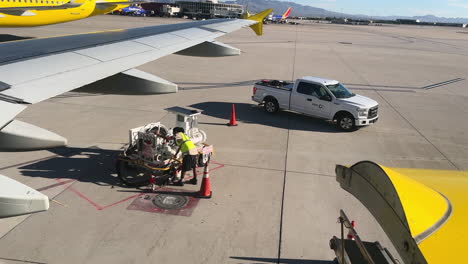 Ground-crew-checks-refueling-lines-on-tarmac-at-Las-Vegas-Airport,-with-planes-and-vehicles-in-view