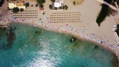Playa-De-Canyamel-Mit-Sonnenschirmen,-Badegästen-Und-Klarem,-Blauem-Wasser,-Sonniger-Tag,-Luftaufnahme