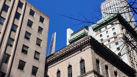 A-low-angle-view,-looking-up-at-the-tall-skyscrapers-in-New-York-City-from-5th-Avenue-on-a-sunny-day-with-clear-blue-skies