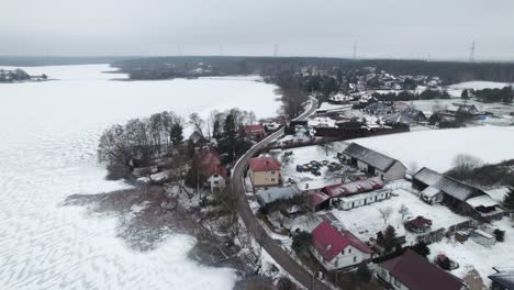 Rural-polish-village-on-a-frozen-lake-in-Winter,-snowy-countryside,-aerial-dolly