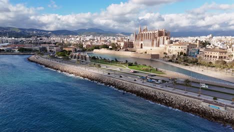 Cathedral-de-mallorca-overlooking-the-sea-with-city-backdrop,-sunny-day,-aerial-view