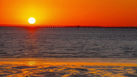 Atemberaubende-Aussicht-Auf-Den-Strand-Mit-Der-Sonne,-Die-Am-Horizont-Aufgeht,-Menschen,-Die-Sich-Neben-Dem-Meer-Aufwärmen