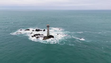 Flug-In-Richtung-Hanois-Leuchtturm-Guernsey-Raus-Aufs-Meer-An-Einem-Hellen-Bewölkten-Tag-Mit-Felsen-Und-Gischt-Und-Schäumenden-Wellen