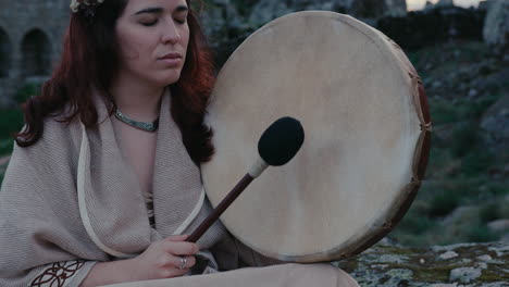 Spirituelle-Frau,-Die-Friedlich-Eine-Schamanische-Trommel-In-Einem-Wunderschönen-Mittelalterlichen-Dorf-Spielt,-Nahaufnahme