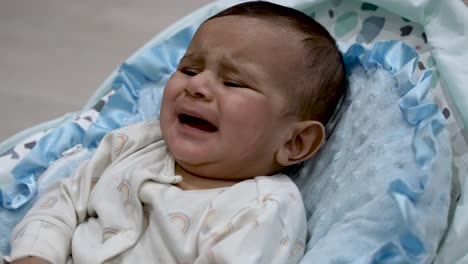 British-Asian-6-Month-Old-Baby-Crying-And-Looking-Agitated-Whilst-In-Baby-Bouncer