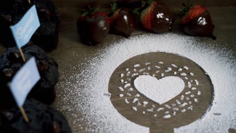 Making-a-heart-out-of-white-confectionate-powdered-sugar-with-chocolate-covered-strawberries-and-muffins-on-the-side