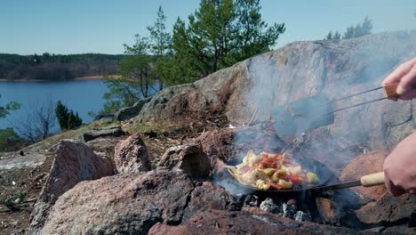 Hands-cooking-food-on-campfire-frying-pan-a-sunny-day