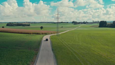 Car-driving-on-a-country-road-amid-green-fields,-sunny-day,-aerial-shot