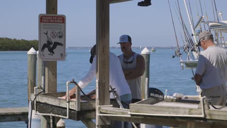 Hombres-Cortando-Pescado-En-La-Estación-De-Limpieza-En-El-Muelle-Y-Arrojando-Restos-Al-Océano-A-Pelícanos-Sin-Señal-De-Alimentación-En-Florida