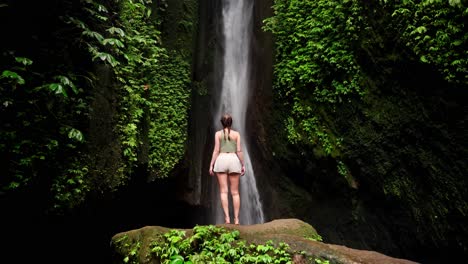 Young-woman-stands-mesmerized-by-the-cascading-waterfall-before-her
