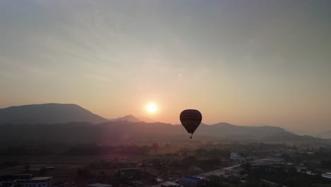 Heißluftballon-Fliegt-Bei-Goldenem-Sonnenaufgang-über-Einem-Dorf-Mit-Bergigem-Hintergrund