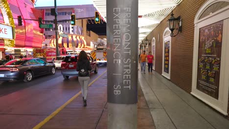 Tilt-Up-View-From-Pavement-To-Reveal-Female-Tourist-Walking-Past-Lamppost-With-Sign-Saying-Fremont-Street-Experience-In-Las-Vegas