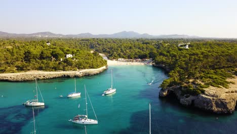 Cala-mondrago-beach-with-anchored-yachts,-turquoise-waters,-and-lush-greenery,-aerial-view,-in-Mallorca,-Spain,-in-the-Mediterranean-Sea
