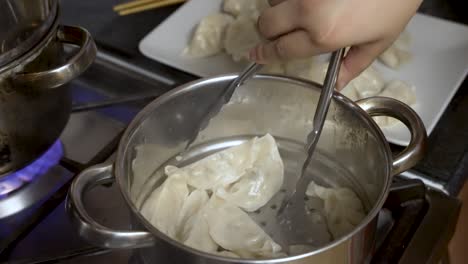 Steaming-dumplings-in-metal-steamer-over-pot-on-stove,-hand-with-tongs-serving