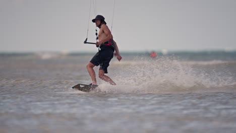 Lose-up-panning-shot-of-a-kiteboarder-skimming-across-the-water-without-a-shirt-and-in-shorts-and-hat-before-executing-a-tight-turn,-slow-motion