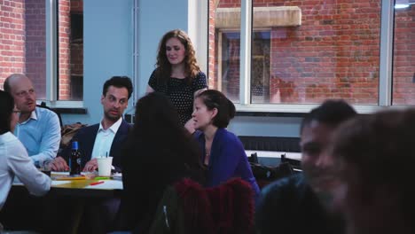 Woman-with-curly-hairs-listing-to-group-of-young-adults-discussing-at-table