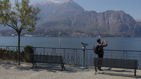 Ciudad-De-Bellagio,-Lombardía,-Italia---Un-Turista-Que-Captura-El-Lago-Como-Desde-La-Famosa-Pasarela-Deungolago-Europa---Toma-Panorámica-Aérea