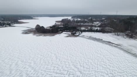 Aerial-establisher-polish-countryside-in-Winter,-frozen-lake-on-a-cloudy-day