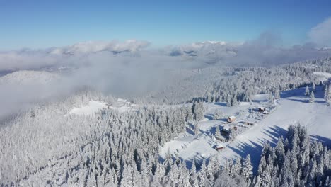 Snow-covered-bucegi-mountains-with-clouds-and-trees,-aerial-view