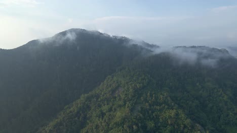 Drone-fly-ascending-over-forest-and-hill-with-dramatic-fog-shrouded-the-peak