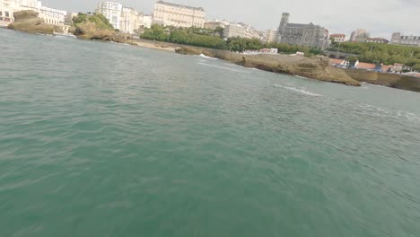 Freestyle-Drohne-Fliegt-In-Geringer-Höhe-Um-Die-Felsen-Von-Port-Des-Pecheurs-Oder-Fischerhafen-Mit-Der-Stadt-Im-Hintergrund,-Biarritz-In-Frankreich