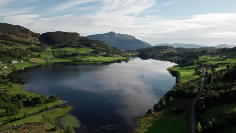 Aerial-shot,-climbing-over-a-small-lake-surrounded-by-lush-green-fields-and-forest