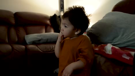 An-18-month-old-baby-boy-watches-TV-in-the-evening,-captivated-by-the-screen-and-sucking-his-fingers