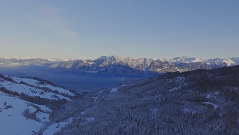 Drone-view-of-the-dawn-sky-casting-a-silhouette-over-snowy-mountains