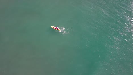 Un-Surfista-Solitario-Sobre-Una-Tabla-Colorida-En-Las-Cristalinas-Aguas-De-Port-Ginesta,-Barcelona,-Vista-Aérea