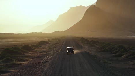 Impresionante-Puesta-De-Sol-Con-Jeep-En-Un-Camino-De-Tierra-En-La-Costa-Montañosa-De-Islandia,-Aéreo