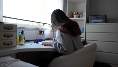 Rear-shot-of-a-young-woman-studying-at-a-desk-by-the-window,-4K