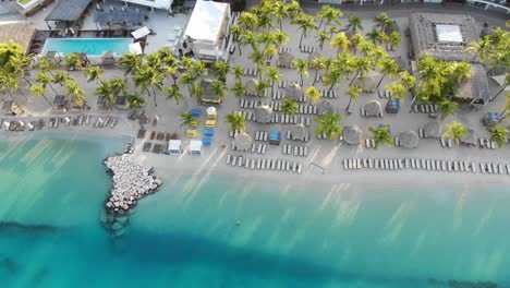 Sunbeds-on-beach-by-resort-at-Mambo-Beach-on-Curaçao,-overhead-aerial