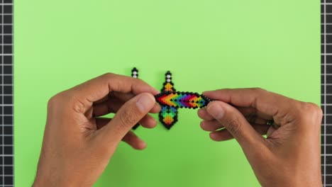 Hand-arranging-colorful-bead-earrings-on-a-green-background,-craft-concept