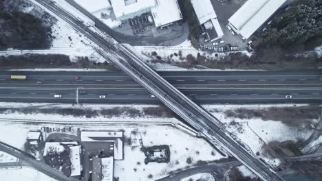 train-passing-over-highway-bridge,-winter,-top-down-droneshot,-aerial,-austria