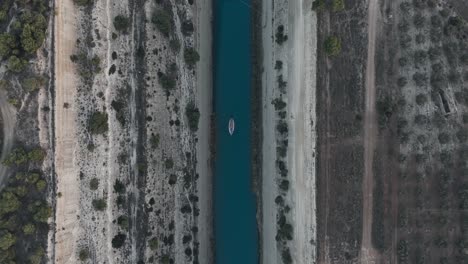 Boat-crossing-the-Corinth-Isthmus-from-a-drone's-perspective,-providing-a-unique-view-of-the-narrow-land-strip